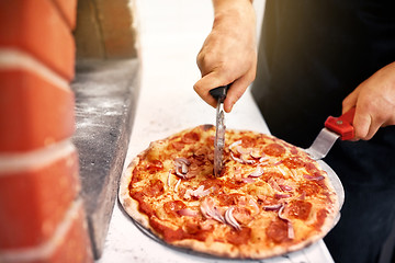 Image showing cook hands cutting pizza to pieces at pizzeria