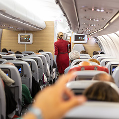 Image showing Interior of commercial airplane with stewardess walking the aisle.