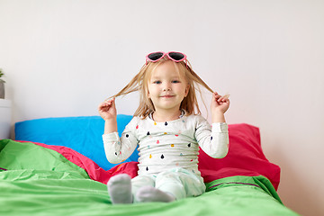 Image showing smiling little girl with sunglasses on bed at home