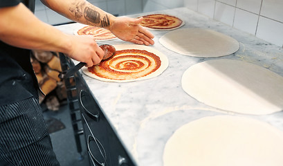 Image showing cook applying tomato sauce to pizza at pizzeria