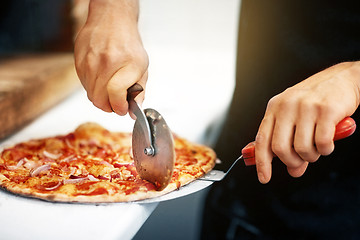 Image showing cook hands cutting pizza to pieces at pizzeria