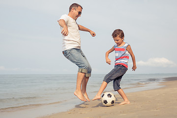 Image showing Father and son playing football on the beach at the day time.