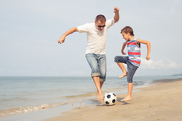 Image showing Father and son playing football on the beach at the day time.