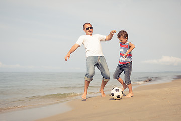 Image showing Father and son playing football on the beach at the day time.