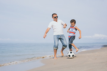 Image showing Father and son playing football on the beach at the day time.