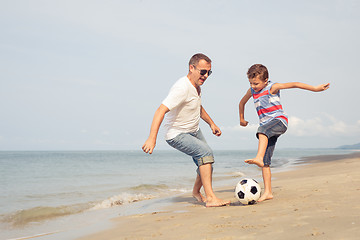 Image showing Father and son playing football on the beach at the day time.