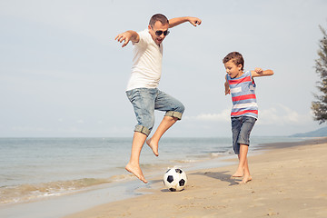 Image showing Father and son playing football on the beach at the day time.