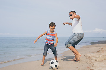 Image showing Father and son playing football on the beach at the day time.