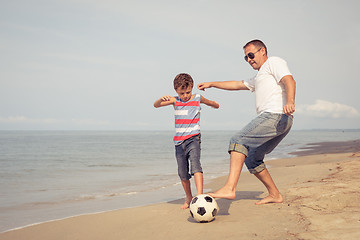 Image showing Father and son playing football on the beach at the day time.