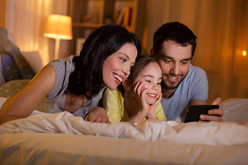 Image showing happy family with smartphone in bed at night