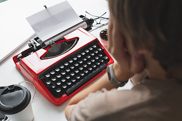 Image showing Woman writer thoughtfully working on a book on her Desk red typewriter