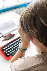 Image showing Woman writer thoughtfully working on a book on her Desk red typewriter