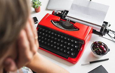 Image showing Woman writer thoughtfully working on a book on her Desk red typewriter