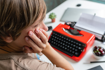 Image showing Woman writer thoughtfully working on a book on her Desk red typewriter