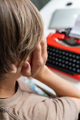 Image showing Woman writer thoughtfully working on a book on her Desk red typewriter