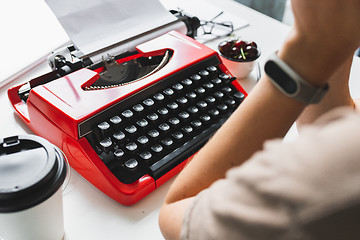 Image showing Woman writer thoughtfully working on a book on her Desk red typewriter