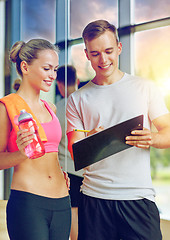 Image showing smiling young woman with personal trainer in gym