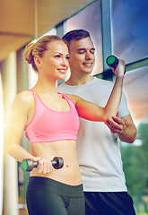 Image showing smiling young woman with personal trainer in gym