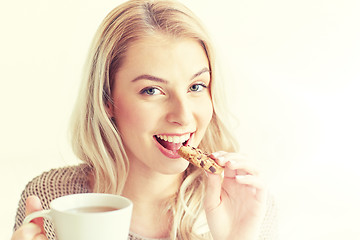 Image showing happy woman with tea eating cookie at home