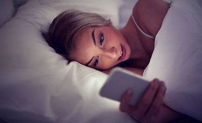 Image showing young woman with smartphone in bed at home bedroom