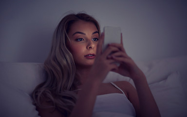 Image showing young woman with smartphone in bed at home bedroom