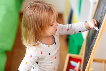 Image showing happy little girl drawing on chalk board at home