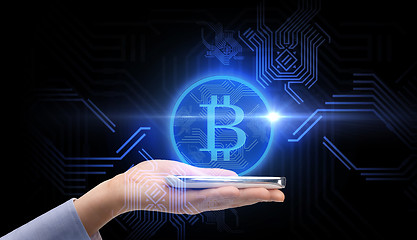 Image showing close up of hand with smartphone and bitcoin