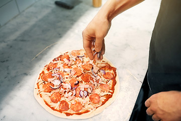 Image showing cook adding onion to salami pizza at pizzeria