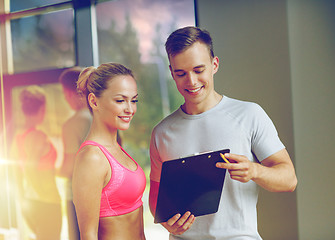 Image showing smiling young woman with personal trainer in gym