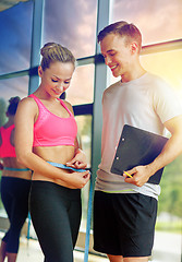 Image showing smiling young woman with personal trainer in gym
