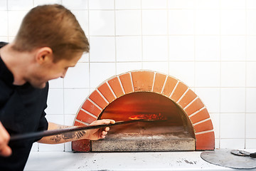 Image showing man with peel placing pizza to oven at pizzeria