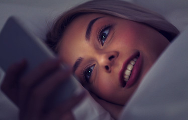 Image showing young woman with smartphone in bed at night