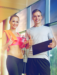 Image showing smiling young woman with personal trainer in gym