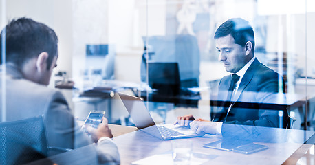 Image showing Two young businessmen using laptop computer at business meeting.