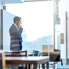 Image showing Businessman talking on a mobile phone while looking through window.