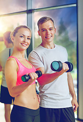 Image showing smiling young woman with personal trainer in gym