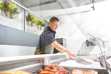 Image showing male seller adding ice to fridge at fish shop