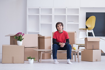 Image showing boy sitting on the table with cardboard boxes around him