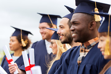 Image showing happy students in mortar boards with diplomas