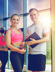 Image showing smiling young woman with personal trainer in gym