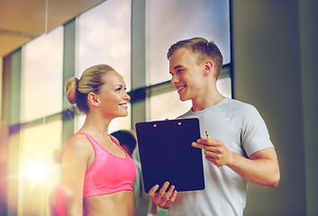 Image showing smiling young woman with personal trainer in gym