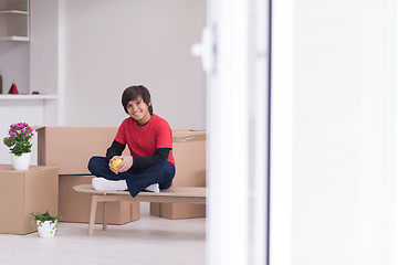 Image showing boy sitting on the table with cardboard boxes around him