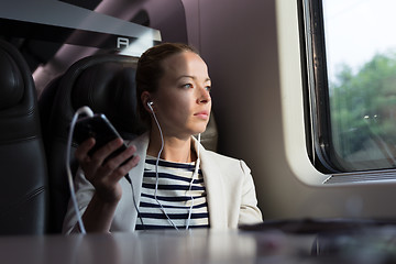 Image showing Thoughtful businesswoman listening to podcast on mobile phone while traveling by train.