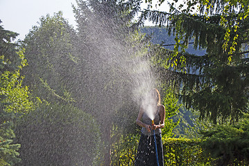 Image showing A young woman Watering a lawn in the yard of the house, a backgr