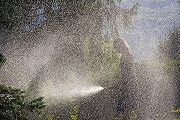 Image showing A young woman Watering a lawn in the yard of the house, a backgr