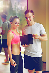 Image showing smiling young woman with personal trainer in gym