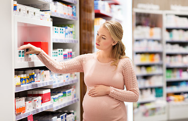 Image showing happy pregnant woman with medication at pharmacy