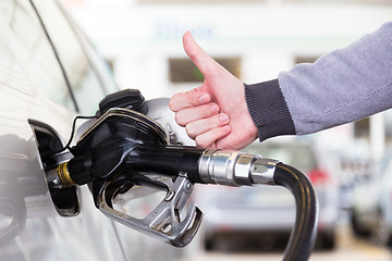 Image showing Petrol or gasoline being pumped into a motor vehicle car. Closeup of man, showing thumb up gesture, pumping gasoline fuel in car at gas station.