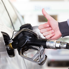 Image showing Petrol or gasoline being pumped into a motor vehicle car. Closeup of man, showing thumb up gesture, pumping gasoline fuel in car at gas station.