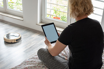 Image showing Vacuum cleaning robot with woman reading